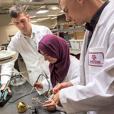 three Engineering Medical students using a soldering iron and electrical equipment in a lab