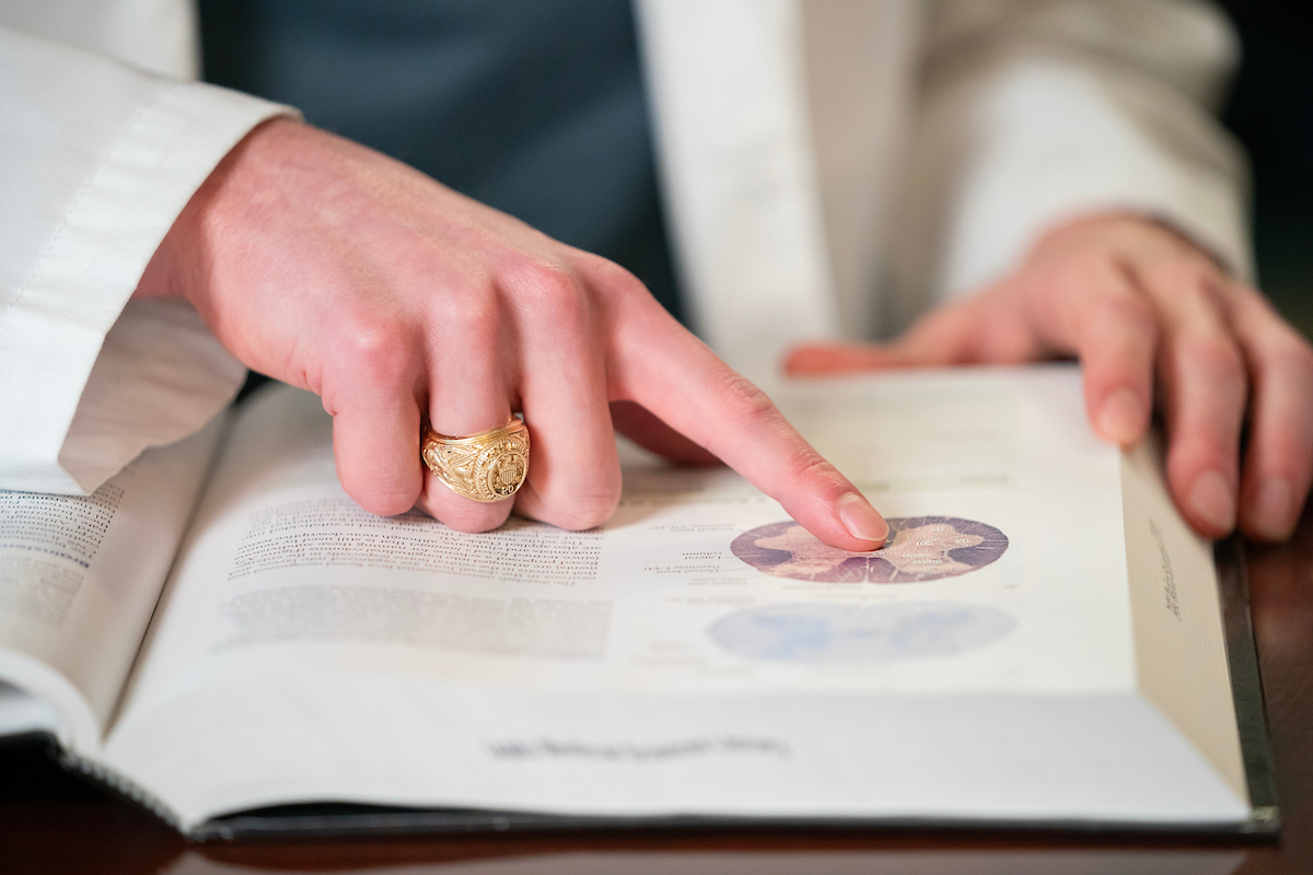 Close-up of a hand wearing an Aggie Ring pointing to an anatomical diagram in a medical textbook.